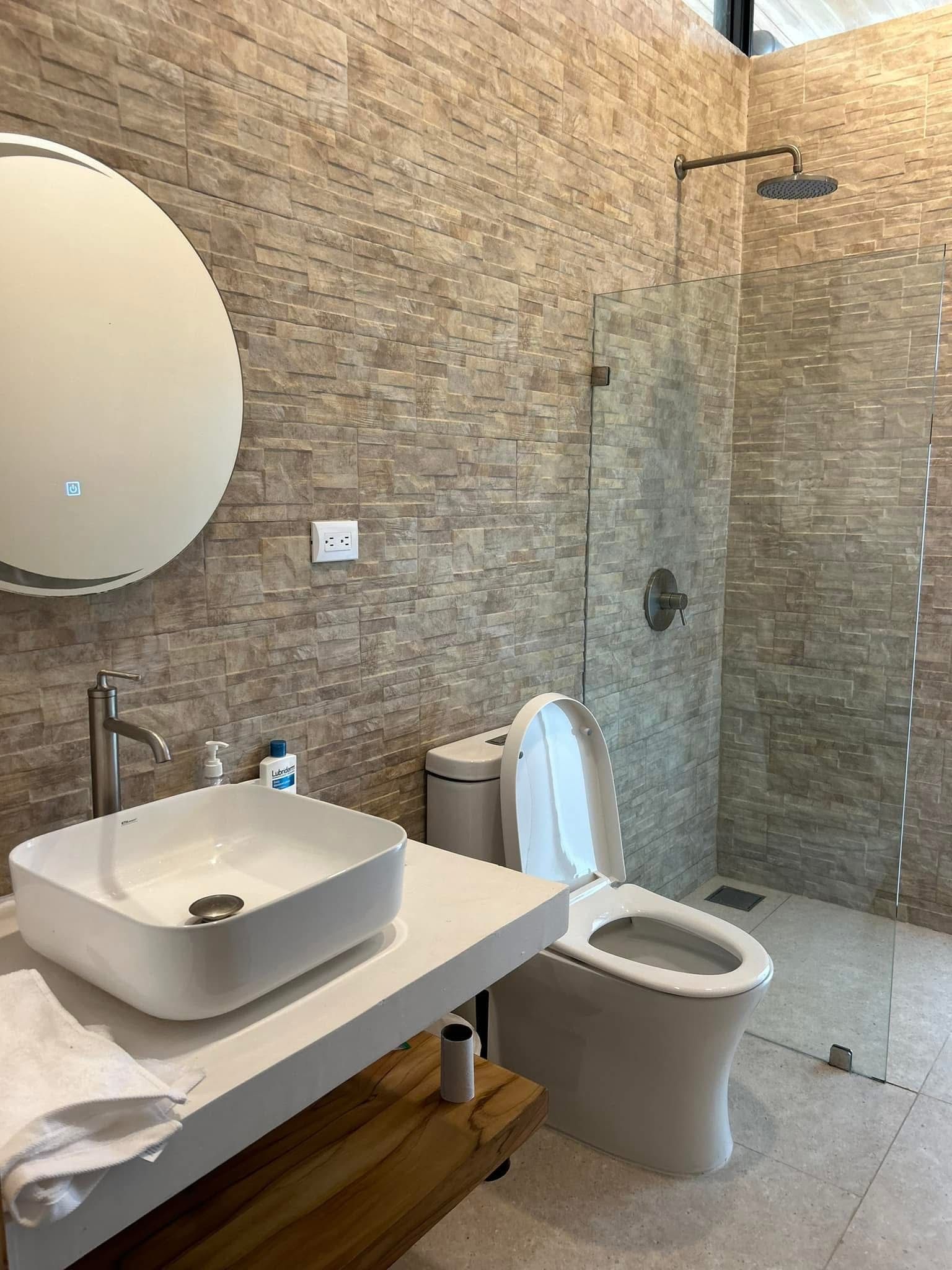 Casa Delicias bathroom clad in natural stone tile with a vessel sink, open shower, and teak-slat ceiling.
