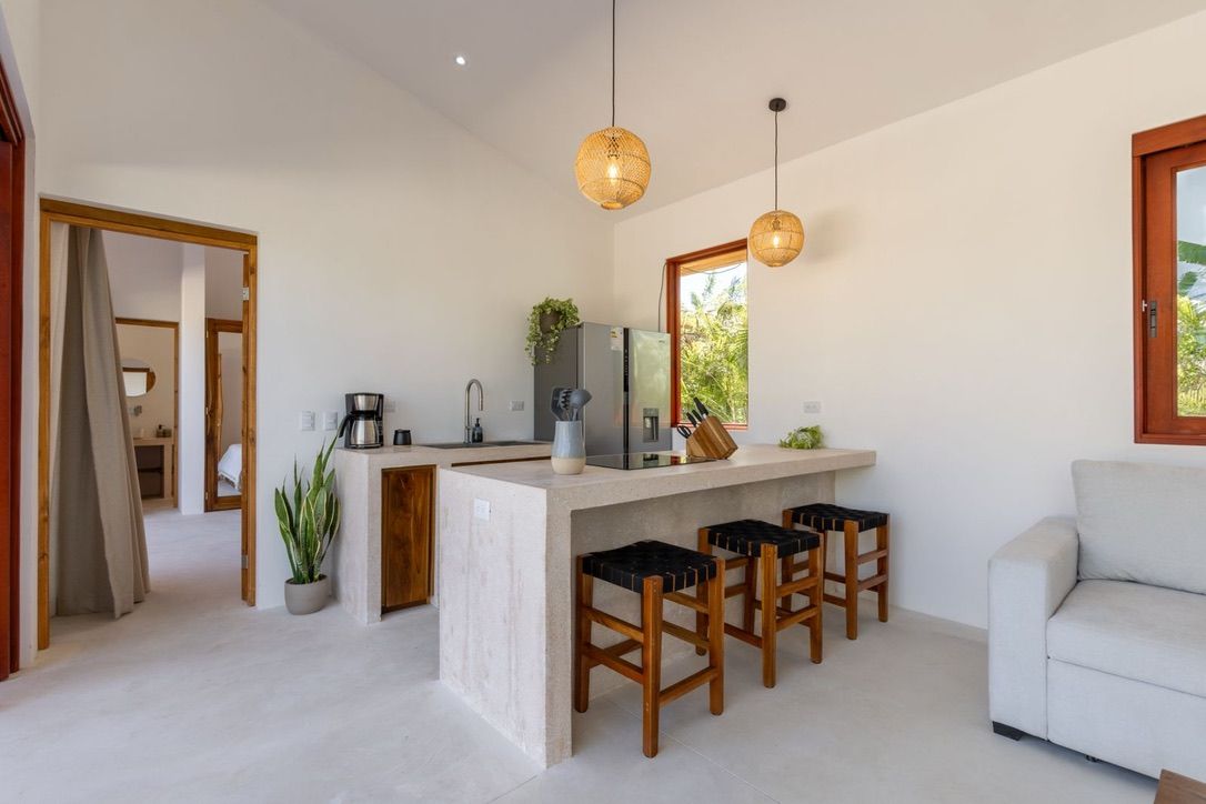 Proyecto Santiago apartment — open kitchen with concrete bar, woven pendant lights, and a view through to the bedroom.